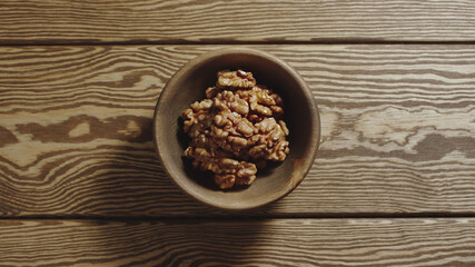 TOP VIEW: Peeled walnuts fill wooden cup on a wooden table