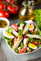 Fresh healthy vegetable salad made of cherry tomato, ruccola, arugula, feta, olives, cucumbers, onion and spices. Greek, Caesar salad in a white bowl on wooden background. Healthy food concept.