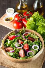 Fresh healthy vegetable salad made of cherry tomato, ruccola, arugula, feta, olives, cucumbers, onion and spices. Greek, Caesar salad in a white bowl on wooden background. Healthy food concept.