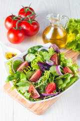 Fresh healthy vegetable salad made of cherry tomato, ruccola, arugula, feta, olives, cucumbers, onion and spices. Greek, Caesar salad in a white bowl on wooden background. Healthy food concept.