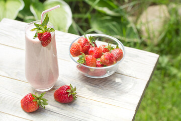 A milkshake made from fresh strawberries stands on a light wooden background , with green grass visible in the right corner