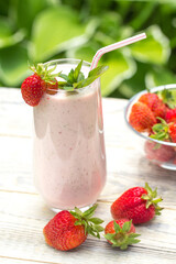 A milkshake of fresh strawberries stands on a light wooden background , strawberry berries are on the table and in a transparent vase