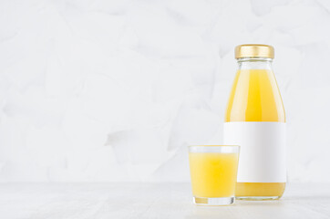 Fresh orange juice in glass bottle with blank label mock up with wine glass on wood table in soft light white interior, template for packaging, advertising, design product, branding identity.