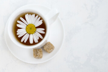 Obraz na płótnie Canvas A flower of chamomile in a white porcelain cup with tea on a light background. Herbal tea, herbal treatment, alternative medicine. Horizontal orientation, top view. Copy space.