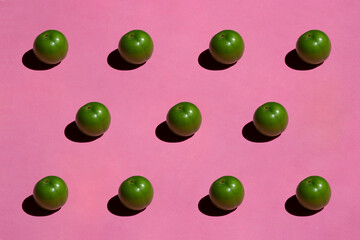 Green plum isolated on pink background. Still life photography.
