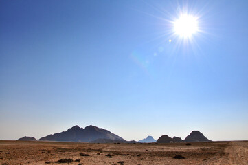 Minimalist landscape of harsh hot desert with Spitzkoppe Mountains on the horizon, vivid blue no clouds sky and sun shining, Namibia, Africa