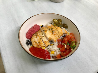 Traditional Jamaican Food Bowl with Chicken, Red Kidney Beans, Beet Sauce, Basmati Rice Pilaf, Avocado Guacamole, Jalapeno Pepper and Coconut Milk at Local Restaurant.