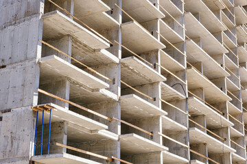 Detail of residential building under construction. Concrete structure with metal struts and temporary wooden railings. High-rise residential building under construction against a blue sky with clouds