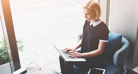 Young successful businesswoman is publishing an advertisement on the Internet via portable laptop computer about search for specialists in the economic field,while is sitting in modern co-working cafe