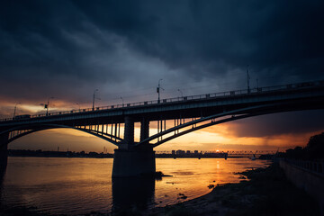 Fototapeta na wymiar Urban evening landscape. Road bridge over the Ob river at sunset. Fantastic clouds in the dark sky.