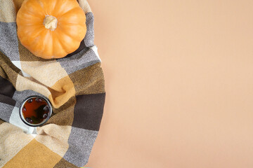 Pumpkin, plaid, dry autumn leaves, cones and tea on a pastel beige background. Autumn minimalism concept, banner. Flat bed, top view, flat lay.