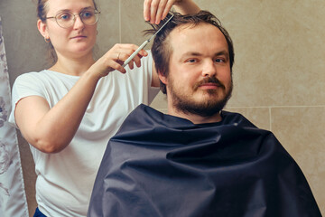 A woman cuts a man's hair with scissors, close-up. The concept of closed salons and barbershop during the isolation of coronavirus