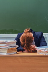 The woman teacher put her head in hands and cries at the blackboard. School teacher in stress sitting at a desk with books