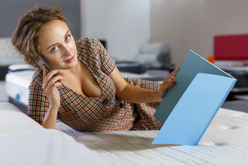 Glad woman lying on bed in mattress store and talking on phone