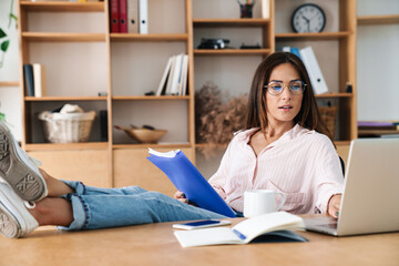 Image of woman working with laptop while sitting with legs on table