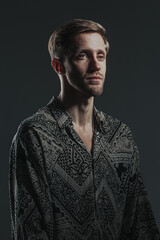 Fototapeta premium Portrait of a handsome caucasian guy in a boho shirt on the black background. Vertical image.