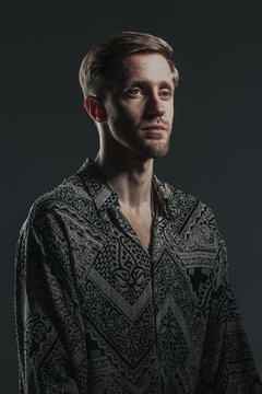 Portrait of a handsome caucasian guy in a boho shirt on the black background. Vertical image.