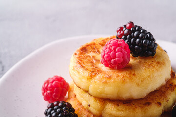 Cottage cheese pancakes, curd fritters dessert with raspberry and blackberry berries in plate on stone concrete background, angle view macro