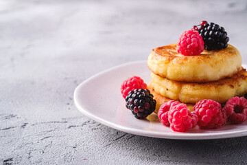Cottage cheese pancakes, curd fritters dessert with raspberry and blackberry berries in plate on stone concrete background, angle view macro