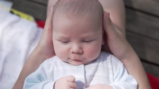 Close-up of cute infant baby Boy in mom's arms. Mom strokes baby on spout and cheeks