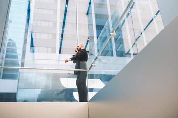 View from below of young male financier dressed in luxury suit is phoning via cell telephone during...