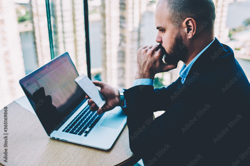 Poster serious bearded entrepreneur with digital smartphone in hands waiting for sms with code to making re