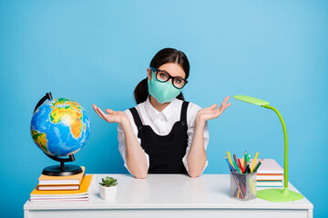 Photo of frustrated girl college student sit table shrug shoulders dont know when quarantine end wear white blouse black overall uniform medical mask isolated over blue color background