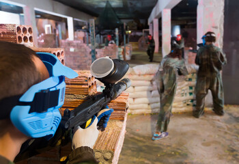 .Rivals are targeting in enemy behind barricades in battlefield in paintball club.