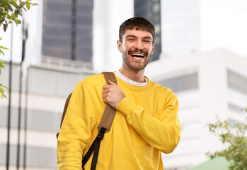 Obraz premium travel, tourism and education concept - happy smiling young man with backpack over city background