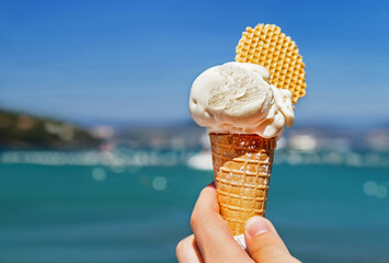 Delicious ice cream cone held up on the blurry sea and sky background. Tasty, sweet food for people...