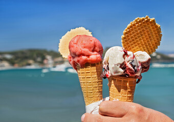 Two delicious ice cream cones held up on the blurry sea and sky background. Tasty, sweet, fresh food for people in the summer.