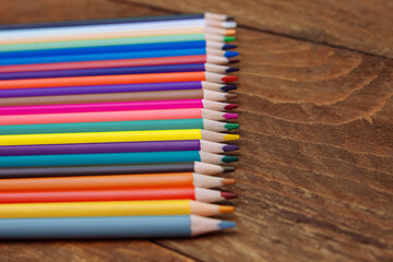 Colored pencils lie in a row on a brown wooden table with an empty space for text, the concept of school education, training and development of children