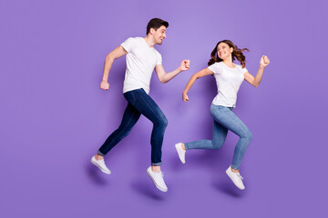 Naklejka na ściany i meble Full size profile photo pretty lady handsome guy jump high sports competition running fast hurry finish line couple race wear casual t-shirts jeans shoes isolated purple color background