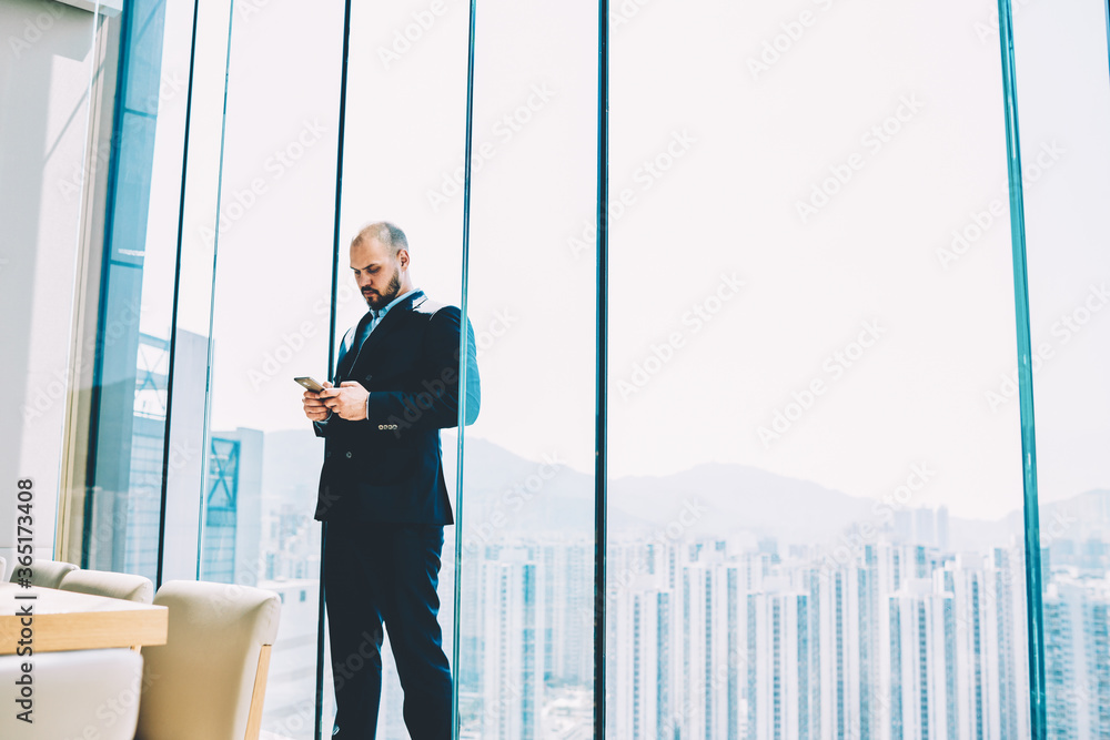 Poster businessman reading news from financial exchange browsing web page on smartphone during break standi