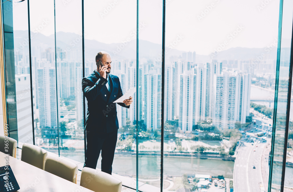 Poster smart financial director in black suit having serious mobile conversation with clients during checki