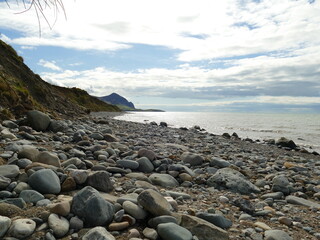 Fototapeta na wymiar Boulder covered seashore and beach with The Rivals Yr Eifl in the background