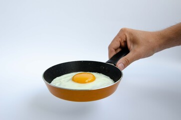 A male hand holds a small children's frying pan with a fried egg
