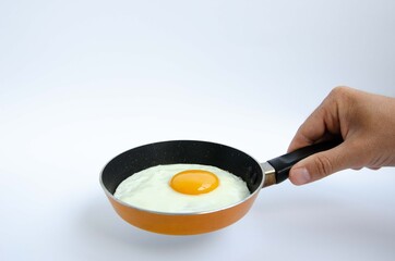 A male hand holds a small children's frying pan with a fried egg