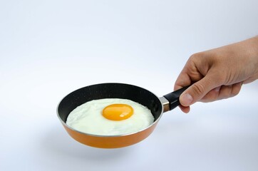 A male hand holds a small children's frying pan with a fried egg