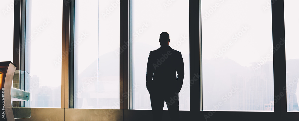 Poster back view of silhouette of young executive manager enjoying scenery out of window and thinking on bu