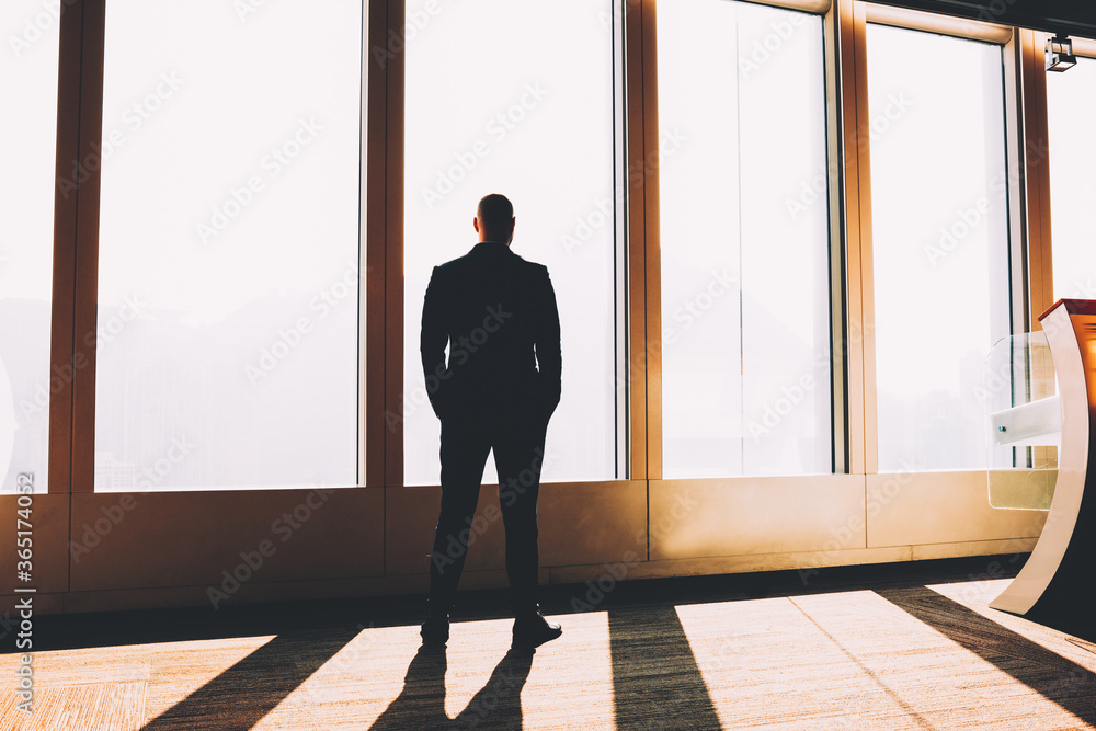 Poster back view of businessman dressed in formal clothes and holding hands in pockets while thinking on cr