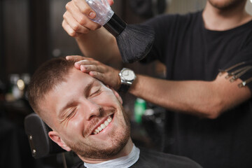 Happy handsome bearded man laughing joyfully, getting powdered after shaving at barbershop