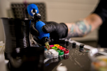 Primer plano de una aguja de tatuar cargando tinta del cubilete de las tintas.