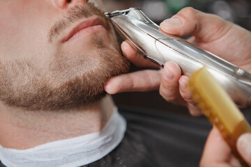 Cropped close up of a barber trimming moustache of male client using electric trimmer