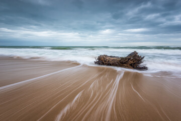 Amazing seascape with stormy morning at a sandy beach and slow shutter and waves flowing out