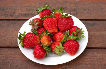 Ripe juicy strawberries on a white plate - a delicious dessert. A wooden background.