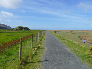 Tarmac footpath crossing a grassy marshy plain with mountains and blue sky in the background near Fairbourne Barmouth Wales
