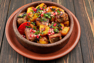 Fried potatoes with meat and pomegranate seeds, in a clay plate, on a wooden background