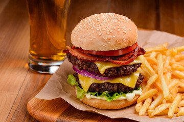 Big double cheeseburger served with handful of French fries and glass of beer