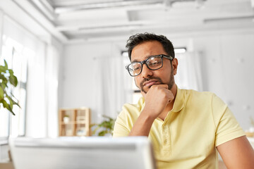 Fototapeta premium remote job, technology and people concept - stressed young indian man in glasses with laptop computer working at home office